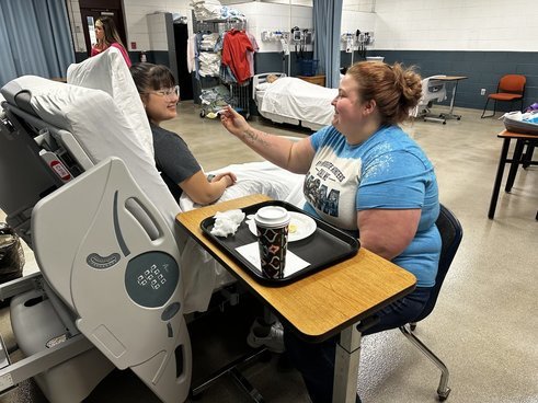 Certified Nurse Aide (CNA) students practice skills such as feeding patients to prepare them for the work they will do upon receiving credentials.